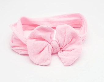 May include: A light pink baby headband with a large bow. The bow is centered on the headband and is made of soft fabric. The headband is designed to be worn around the head.