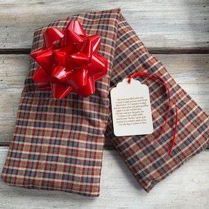 May include: A red and white plaid fabric pouch with a red bow on top. The pouch is tied with a red ribbon and has a white tag attached with the text: "This little bag filled with corn, It made to keep you nice and warm. Microwave it for 2 minutes on high, And say to those aches and pains goodbye. Apply it to the troubled spot, The heat will ease the pain a lot. Or freeze it for a little while, Instead of a compress made of ice. Use this bag as it feels so nice!"