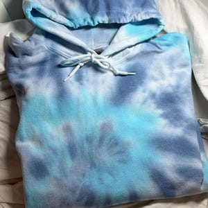 Könnte beinhalten: Ein blaues Spiral-Tie-Dye-Hoodie mit Kapuze und Kordelzug. Der Hoodie ist in Größe S. Der Text "Blues spiral hoodie Size S (UK 8-10)" wird in einem weißen Feld angezeigt. Der Hoodie ist eine Mischung aus Hell- und Dunkelblau.