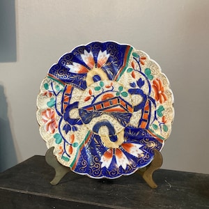 May include: A blue and white porcelain plate with a scalloped edge and a floral design. The plate is decorated with gold accents and features a central motif of a stylized flower.