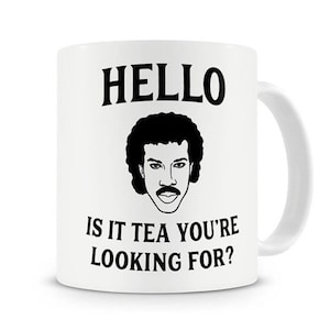 Op de afbeelding: Witte keramische koffiemok met een zwart-witte illustratie van een man met een afro en een snor. De tekst "HELLO IS IT TEA YOU'RE LOOKING FOR?" staat op de mok gedrukt.