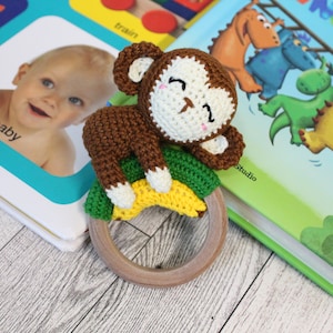 May include: A crocheted monkey toy with a brown and white body, green and yellow banana, and a wooden ring. The toy is lying on top of two children's books.