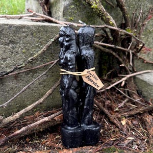 May include: A black candle with two figures, tied together with twine and a tag that reads "Come V Witch Separation". The candle is set against a backdrop of weathered stone, twigs, and moss.