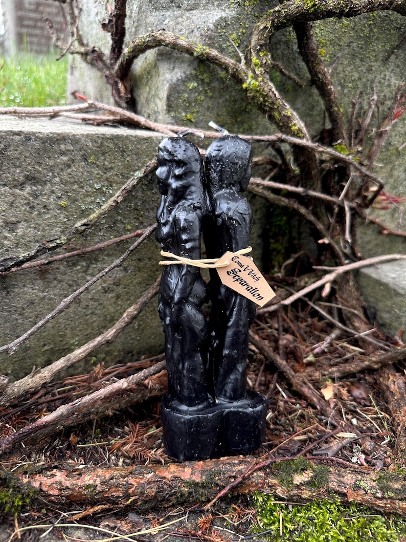 May include: A black candle with two figures, tied together with twine and a tag that reads "Come V Witch Separation". The candle is set against a backdrop of weathered stone, twigs, and moss.