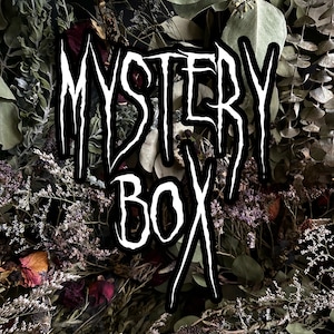 Op de afbeelding: Een wit 'Mystery Box'-bord met een zwarte omtrek is gecentreerd op een achtergrond van gedroogde bloemen en bladeren. De afbeelding toont een verscheidenheid aan gedroogde planten, waaronder eucalyptus en rozen, in tinten groen, bruin en paars.