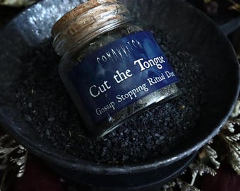 May include: A small glass jar with a cork lid, labeled "Cut the Tongue Gossip Stopping Ritual Dust." The jar sits in a dark, shallow bowl filled with black granules. The label is dark blue with white text.