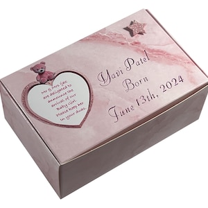 Op de afbeelding: Roze cadeaudoos met een hartvormig ontwerp en een roze teddybeer. De doos heeft de tekst "Mr & Mrs ijaz are delighted to announce the arrival of our Baby Girl. Please keep her in your duas." en "Yavi Patel Born June 13th, 2024".