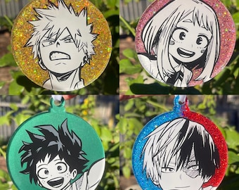 May include: Four round ornaments featuring anime characters. Each ornament has a glittery background in gold, pink, green, and blue. The characters are drawn in black and white. Each ornament has a white ribbon for hanging.