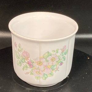 May include: White ceramic planter with a floral design featuring pink and white flowers with green leaves.