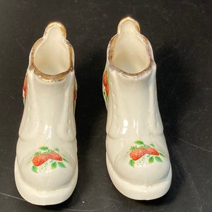 May include: A pair of white ceramic boot-shaped vases with gold trim and a strawberry design.