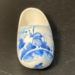 May include: A white ceramic Dutch shoe with blue and white painted details of a windmill and the word "Holland".