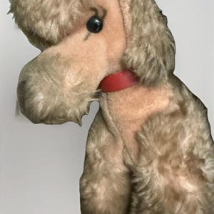Pode incluir: Um brinquedo de pelúcia de poodle vintage com um corpo de pelúcia marrom claro e um rosto rosa. O poodle tem uma coleira vermelha e um olho preto. O brinquedo é feito de material macio e tem um design clássico.