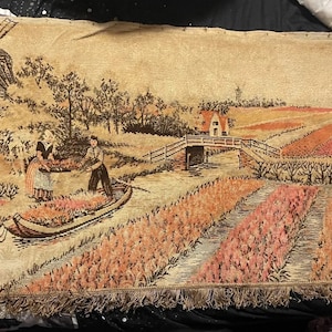 Stary gobelin holenderski (?) w kolorze brązowo-beżowym z motywem ludzi, łodzi, wiatraka, tulipanów, domów, do powieszenia na ścianie