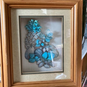 May include: Framed artwork featuring a 3D still life of a pineapple, strawberries, and gourds with blue and green leaves. The artwork is signed "Gloria Fuller" and dated "November 1998".