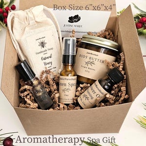 May include: A cardboard gift box measuring 6x6x4 inches containing a collection of skincare products including a cloth bag with oatmeal honey soap, a body butter jar, a linen spray bottle, a body oil roller, and a foaming shower oil bottle.