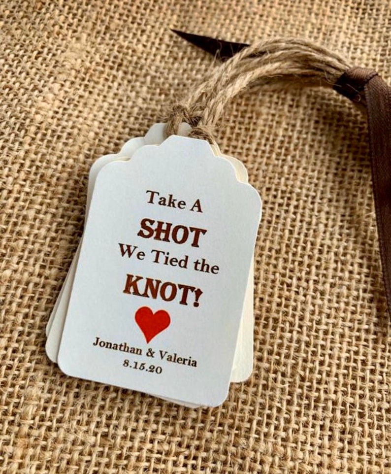 May include: White wedding favor tags with brown text that reads "Take a Shot We Tied the Knot!" with a red heart and the names "Jonathan & Valeria" and the date "8.15.20".