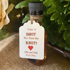 May include: A small bottle of liquor with a white tag that says "Take A SHOT We Tied the KNOT!" with a red heart and the names "Elise and Mike" and the date "04.22.20XX".