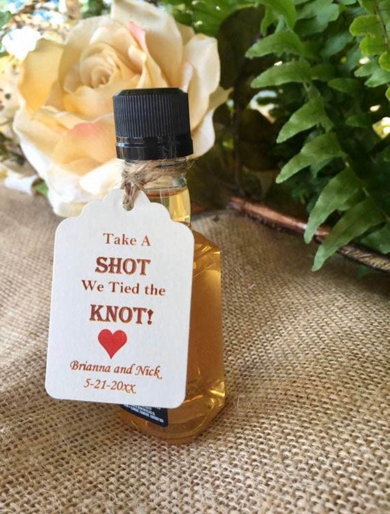 May include: A small bottle of liquor with a white tag that says "Take a Shot We Tied the Knot! Brianna and Nick 5-21-20XX" with a red heart.