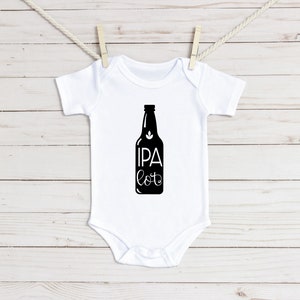 Puede incluir: Un body blanco para bebé con una silueta negra de una botella de cerveza y el texto "IPA lot" impreso en la parte delantera.