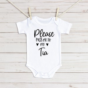 May include: White baby onesie with black text that reads "Please pass me to my Tia" with two hearts around the word "my".