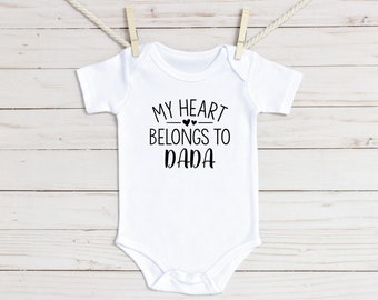 May include: White baby onesie with black text that reads "My heart belongs to Dada" with two small hearts above the word "belongs".