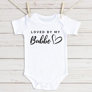 May include: White baby onesie with black text that reads "Loved by my Bubbe" with a heart.