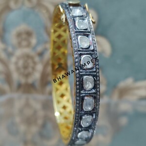 Puede incluir: Un brazalete de oro y plata con una fila de pequeños diamantes redondos engastados en un marco de metal negro. El brazalete está decorado con un patrón repetido de diamantes y metal negro.