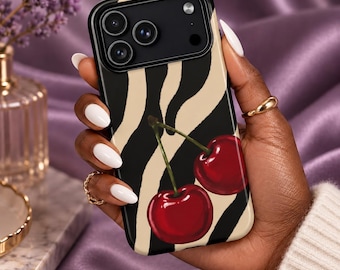 Può includere: Una custodia per smartphone con un motivo a strisce zebrate nere e beige, caratterizzata da un'illustrazione grafica di due ciliegie rosso brillante con piccioli verdi al centro. La custodia presenta un ritaglio nero per la fotocamera a tre lenti.