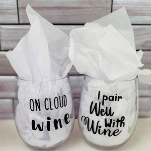 K&ouml;nnte beinhalten: Zwei klare, stiellose Weingl&auml;ser mit schwarzem Text, der &bdquo;ON CLOUD wine&ldquo; und &bdquo;I pair Well With Wine&ldquo; lautet. Jedes Glas ist mit wei&szlig;em Seidenpapier gef&uuml;llt, und der Hintergrund ist ein hellgraues und wei&szlig;es Ziegelmuster.