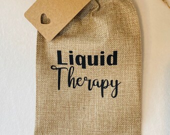 May include: A brown burlap bag with a brown paper tag that says "Liquid Therapy". The bag has a drawstring closure and is tied with a brown twine.