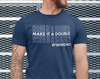 Może przedstawiać: Koszulka w kolorze granatowym z napisem "MAKE IT A DOUBLE" powtórzonym pięć razy w kolorze białym. Tekst jest ułożony pionowo, a hashtag "#TWINDAD" znajduje się na dole koszulki.