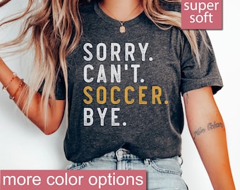 Könnte beinhalten: Ein dunkelgraues Heather-T-Shirt mit dem Text "SORRY. CAN'T. SOCCER. BYE." in weißer und gelber Schrift. Das Shirt ist super weich und in weiteren Farben erhältlich.