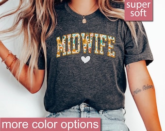 May include: A dark grey heather t-shirt with the word "MIDWIFE" in yellow letters with a floral pattern. The letters are outlined in white. A small white heart is below the word. The t-shirt is super soft and has more color options.