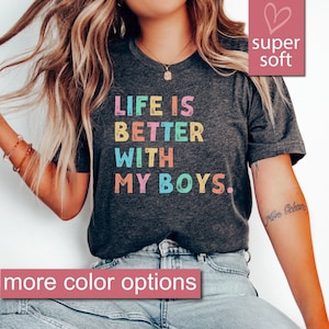 Könnte beinhalten: Ein dunkelgraues Heather-T-Shirt mit dem Text "LIFE IS BETTER WITH MY BOYS." in Regenbogenfarben bedruckt. Das Shirt ist superweich und hat eine lockere Passform.
