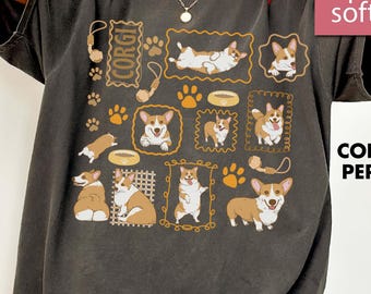 May include: Pepper-colored t-shirt featuring a collection of Corgi illustrations in various poses, framed in gold. The design includes paw prints, dog bowls, and the word "CORGI". The shirt has a "super soft" label.