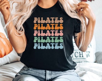 May include: A black t-shirt with the word "PILATES" repeated five times in a rainbow of colors. The text is in a retro, bubble-like font.