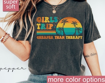 May include: A dark grey t-shirt with a retro sunset graphic and the text "Girls Trip Cheaper Than Therapy".
