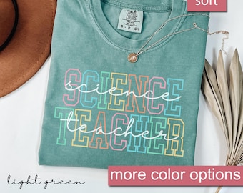 Pode incluir: Uma camiseta verde claro com as palavras "science teacher" em cores do arco-íris. A camiseta é feita de um material macio e confortável.
