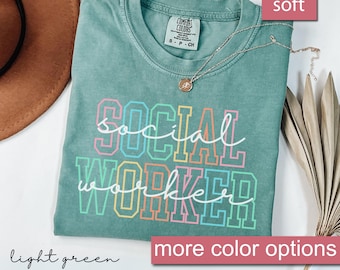 Op de afbeelding: Lichtgroen T-shirt met de tekst "SOCIAL WORKER" in regenboogkleuren. Het shirt is gemaakt van een zachte, comfortabele stof.