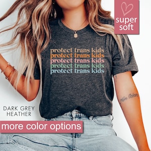 May include: Dark grey heather t-shirt with the text "protect trans kids" repeated five times in rainbow colors. The shirt is super soft and has a relaxed fit.