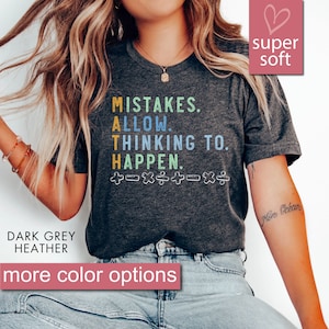May include: A dark grey heather t-shirt with the text "MISTAKES. ALLOW. THINKING TO. HAPPEN." in colourful letters. The text is surrounded by plus, minus, multiplication, and division symbols. The shirt is super soft.