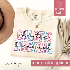 May include: Ivory t-shirt with the text "chaotic bisexual" in colorful block letters. The shirt is super soft and has a tag that says "Comfort Colors".