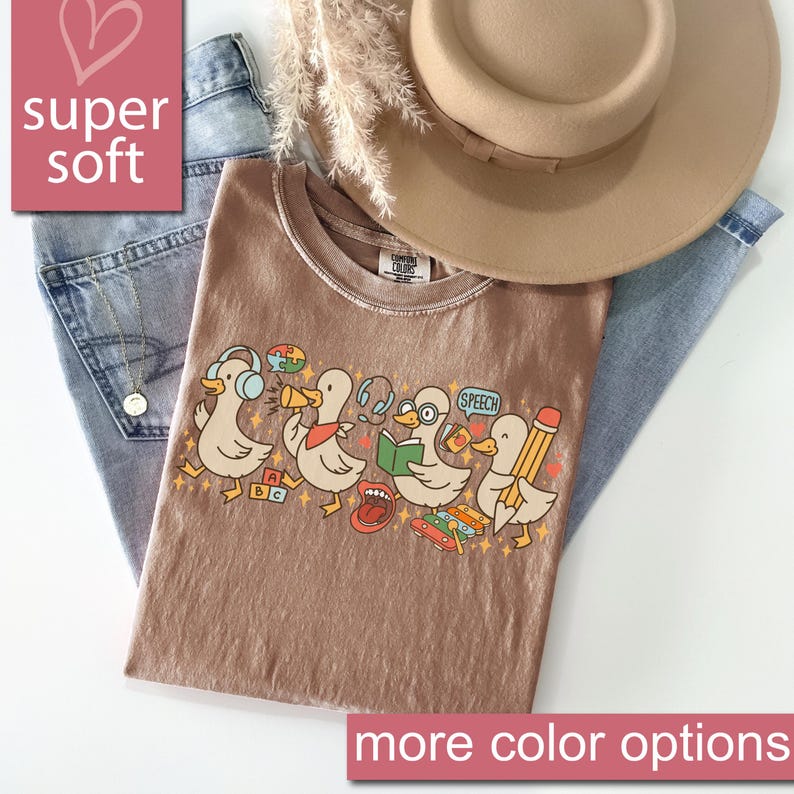 May include: A brown t-shirt with a graphic of cartoon ducks, each with a different accessory, such as headphones and a pencil. The shirt is paired with blue jeans and a tan hat. Text on the shirt includes "SPEECH" and "ABC". The words "super soft" and "more color options" are also visible.
