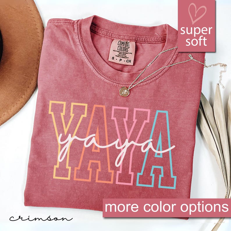 May include: Crimson red t-shirt with the word "YAYA" in rainbow colors. The shirt is made of a soft, comfortable fabric and has a relaxed fit.