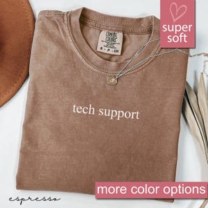 Könnte beinhalten: Espresso-braunes T-Shirt mit dem Text "tech support" in Weiß. Das Shirt ist aus weichem, bequemem Stoff und hat eine lockere Passform.  "Comfort Colors" ist auf dem Etikett aufgedruckt.