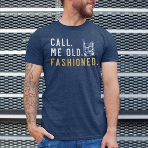 May include: A navy blue t-shirt with the text "CALL ME OLD. FASHIONED." in white and a graphic of an old fashioned cocktail in yellow.