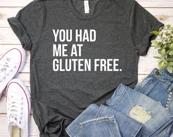 Könnte beinhalten: Ein dunkelgraues T-Shirt mit dem weißen Text "YOU HAD ME AT GLUTEN FREE". Das Bild zeigt blaue Jeans und weiße Leinenschuhe.