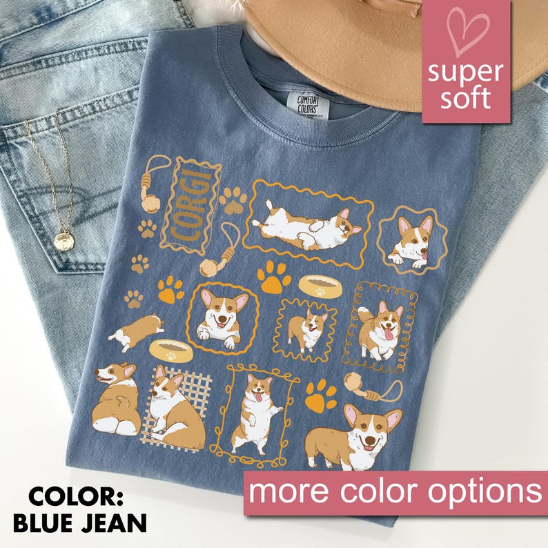 May include: Blue jean colored t-shirt with a repeating pattern of corgi dogs in various poses, paw prints, and dog bones. The word "CORGI" is printed on the shirt. The shirt is labeled "super soft" and "more color options".