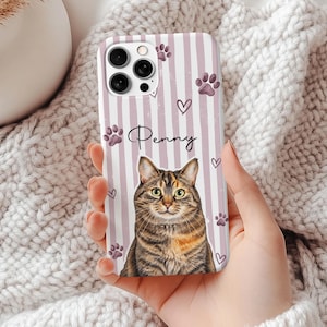 Pode incluir: Uma capa de smartphone com um padrão de riscas verticais rosa claro e branco e uma ilustração central de um gato tigrado castanho. O nome Penny está impresso em letra cursiva preta acima do gato, rodeado por pequenas patas roxas.