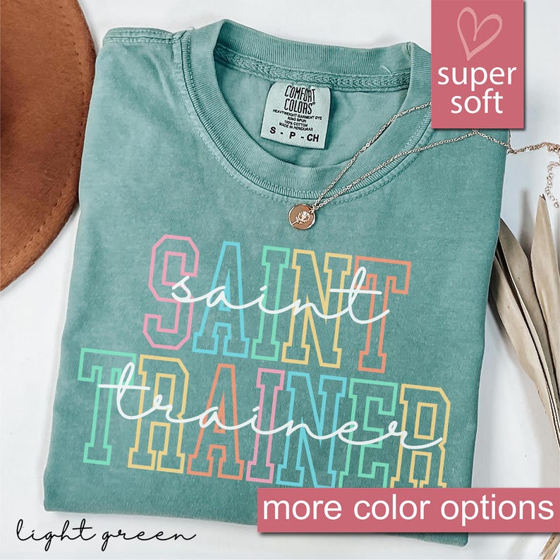May include: A light green t-shirt with the text "Saint Trainer" in rainbow colors. The shirt is made of a soft, comfortable fabric and has a relaxed fit.